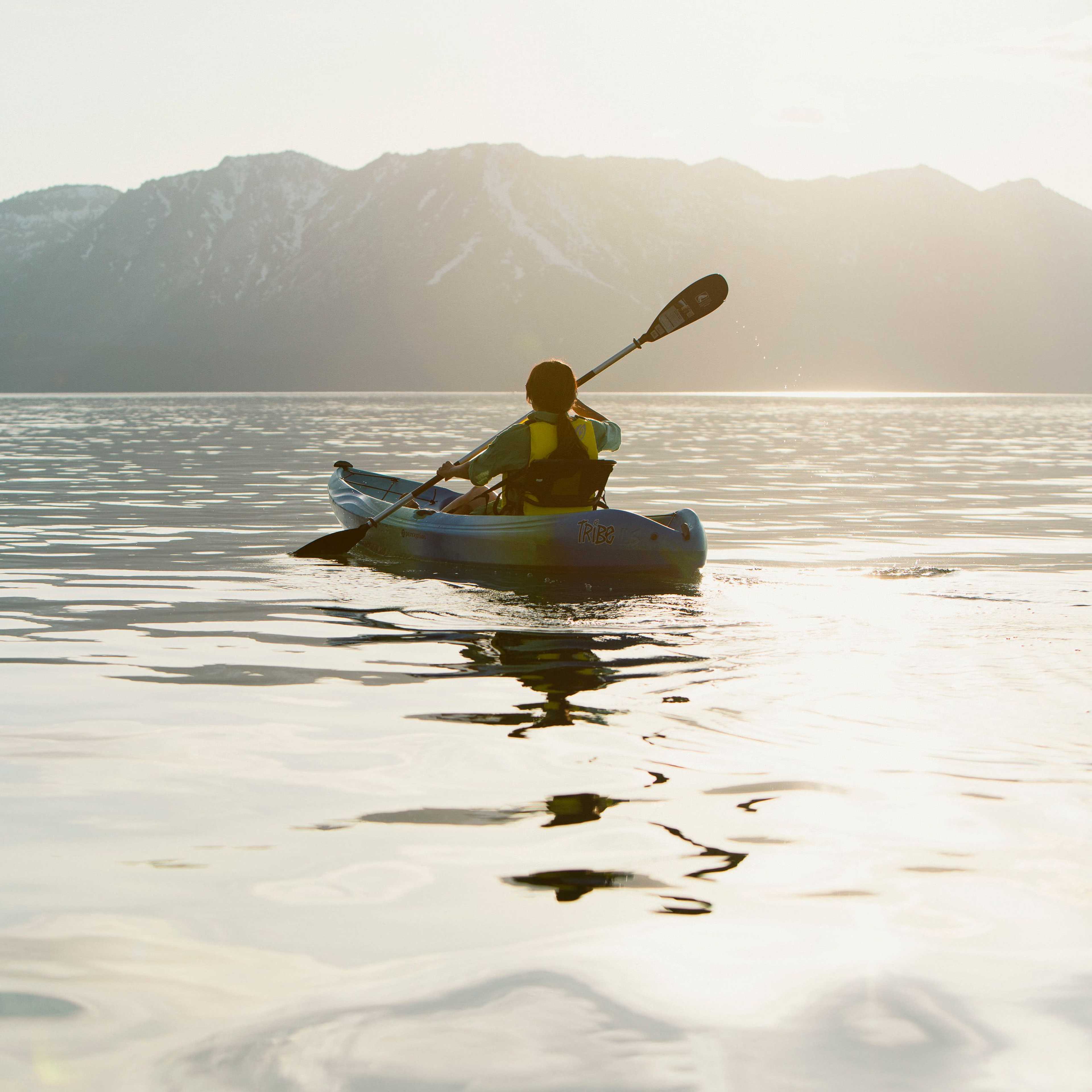 kayaker paddling into the sunset on Lake Tahoe with mountains in the background